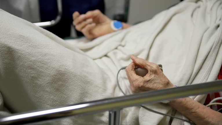 Sairaalasängyssä makaavan ikäihmisen kädet. 