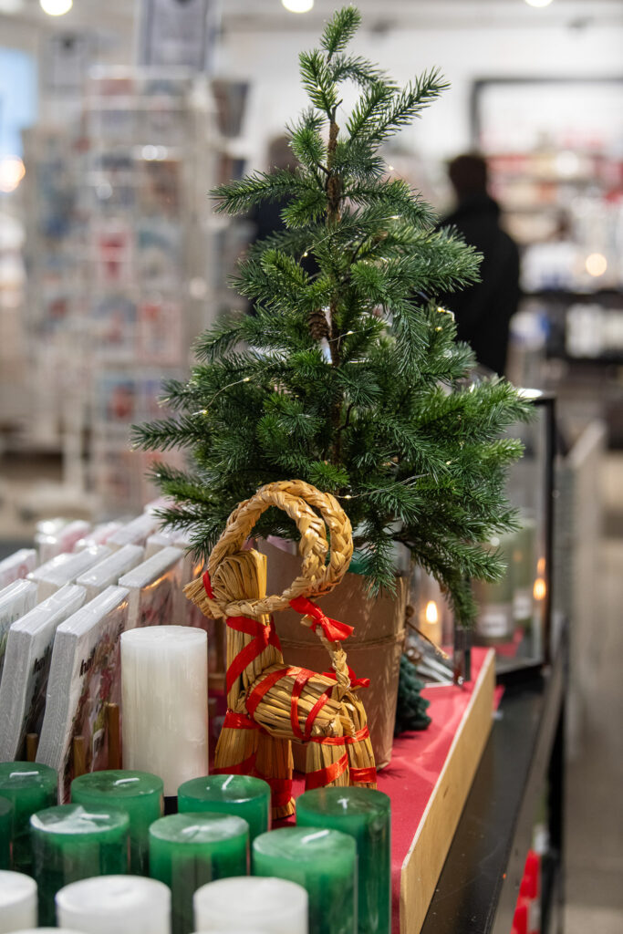 Pöydällä on pieni kuusi, olkipukki ja kynttilölitä. Takana näkyy epätarkkana muita tuotteita.