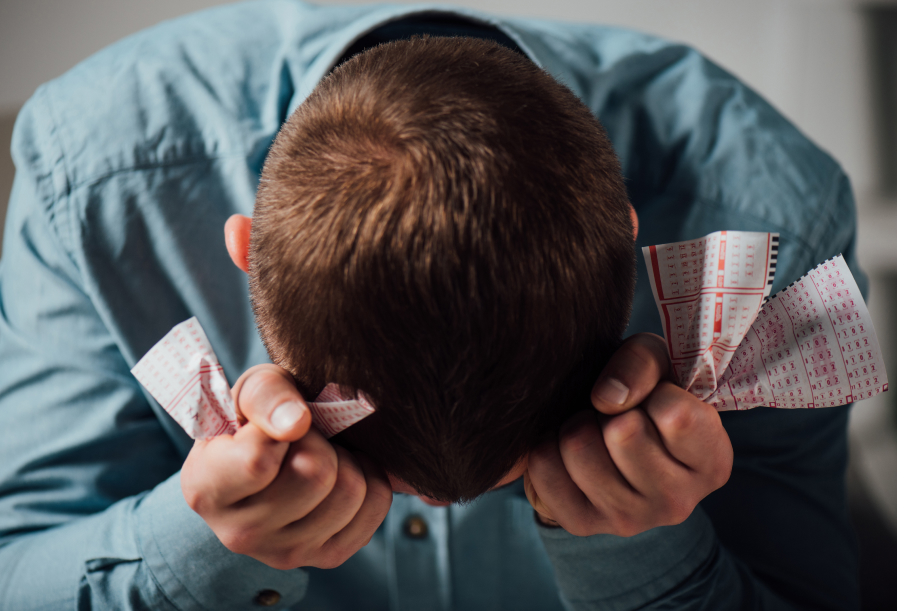 Mies pitää käsissään rypistyneitä lottokuponkeja ja näyttää harmistuneelta.