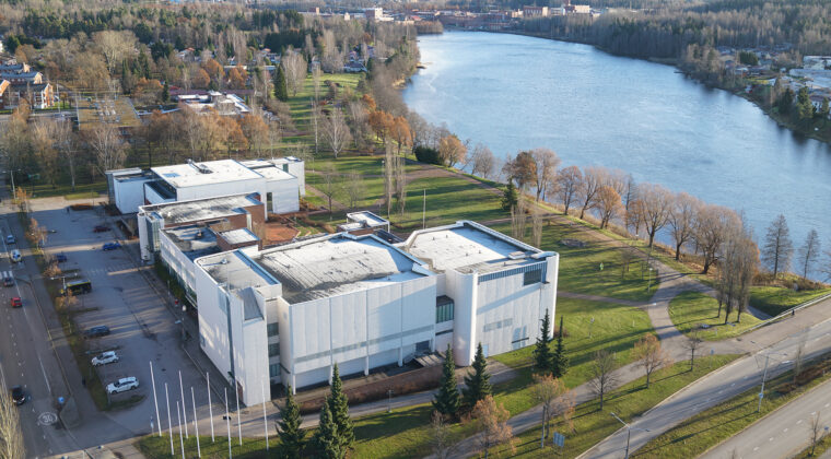 Ilmakuva valkoisesta Kuusankoskitalosta Kymijoen rannassa. Taustalla näkyy UPM Kymmenen paperitehdas.