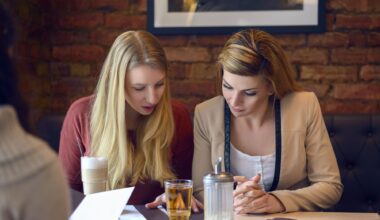 Kaksi vaaleatukkaista naista istuvat pöydän ääressä ja tarkastelevat papereita.