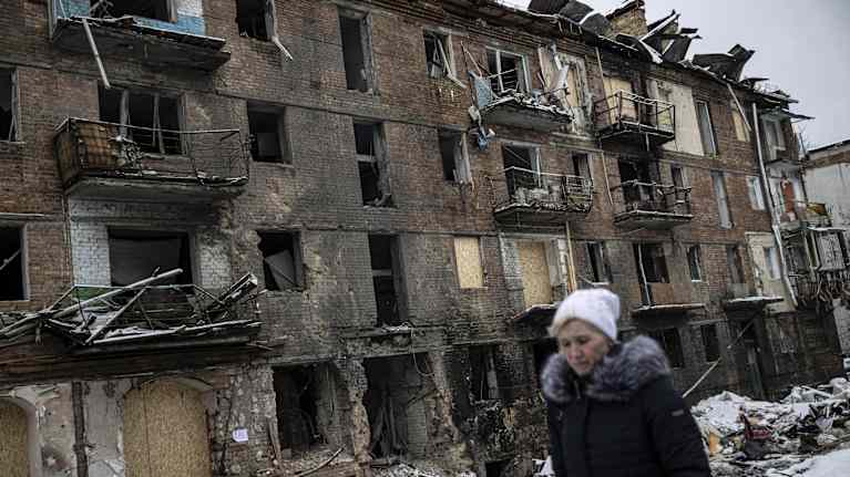 Henkilö kävelee tuhoutuneen kerrostalon edessä.
