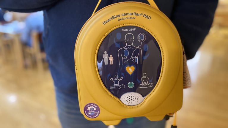 Lähikuva miehen sylissä olevasta keltaisesta defibrillaattorista eli sydäniskurista.