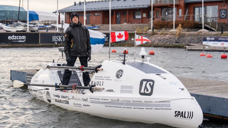 Jari Saario seisoo Atlantin ylityksessä käyttämässään valkoisessa soutuveneessä. Vene on pienvenesataman laiturissa.