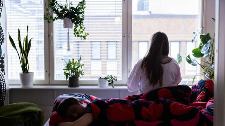 Nainen istuu sängyllä ikkunan edessä ulos katsellen miehen vielä nukkuessa.