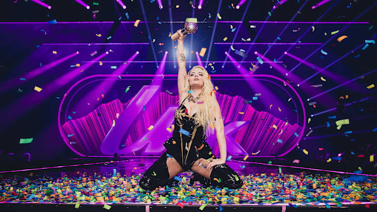 Erika Vikman polvillaan konfettisateessa. Vikman nostaa toisella kädellään UMK-pokaalia ilmaan.