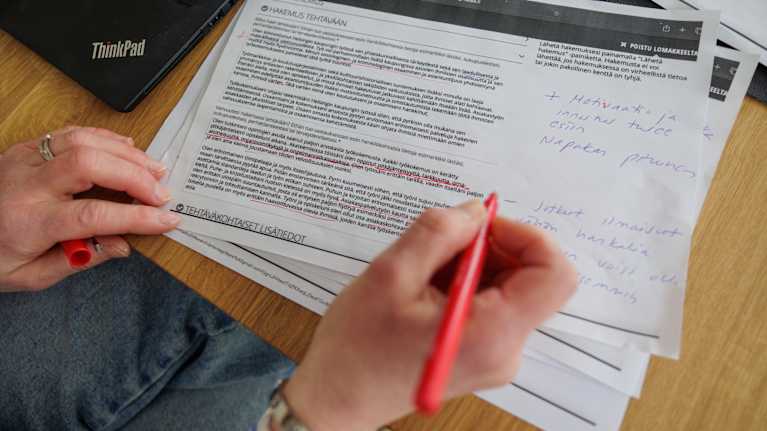 Rekrypomo Heli Lappi-Rantanen tutkii papereita keittiön pöydän ääressä.