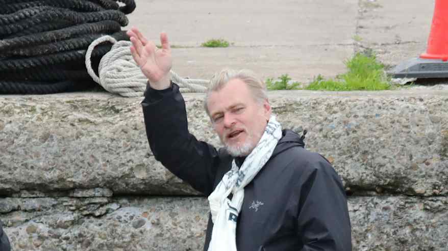 Christopher Nolan heiluttaa kättää sinisessä asussa ulkona.