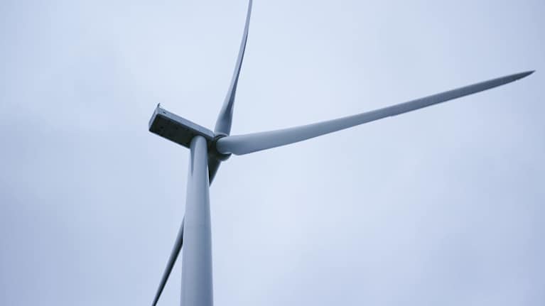 Lähikuva tuulivoimalan roottorista ja lavoista harmaata taivasta vasten.