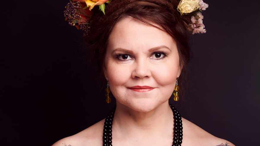 kirjailija Katja Kettu olkapäät paljastavassa mustassa paidassa. Hänellä on ruusutatuonnit olkapäissä ja kukkia hiuksissaan.