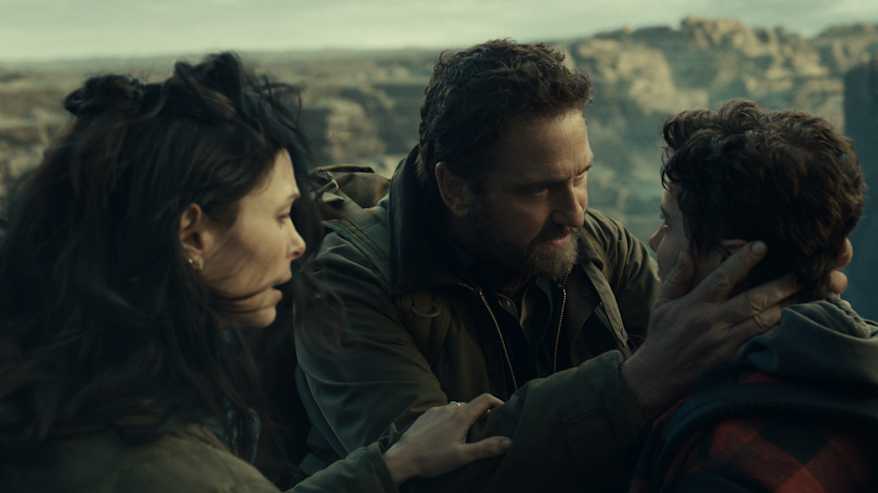 Mies pitelee pojan päätä rakastavasti, vieressä nainen, taustalla rotkomaisema.