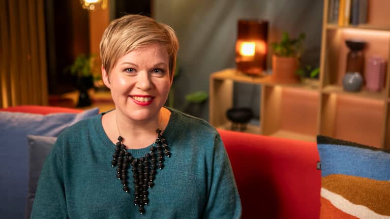 Annika Saarikko hymyilee istuessaan sohvalla.