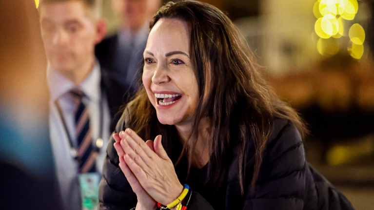 Maria Corina Machado hymyilee ja pitelee käsiään.