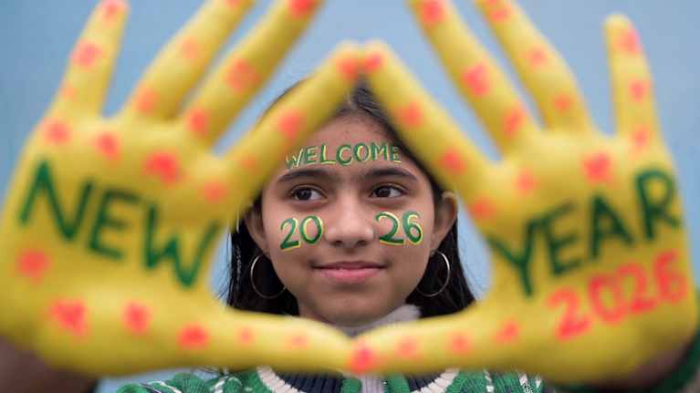 Henkilö näyttää kämmeniään, joissa lukee New Year 2026. Käsien välistä näkyy kasvot, joissa teksti Welcome 2026.