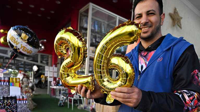 Henkilö pitää käsissään kullanvärisiä numeroilmapalloja, jotka muodostavat luvun 26.