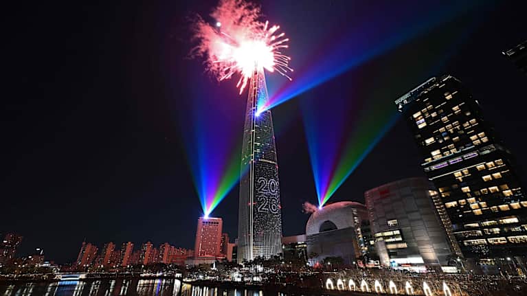 Uudenvuoden ilotulitus valaisee taivaan pilvenpiirtäjän yläpuolella kaupunkimaisemassa.