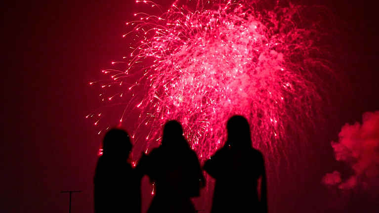 Kolme henkilöä katselee ilotulitusta yötaivaalla.