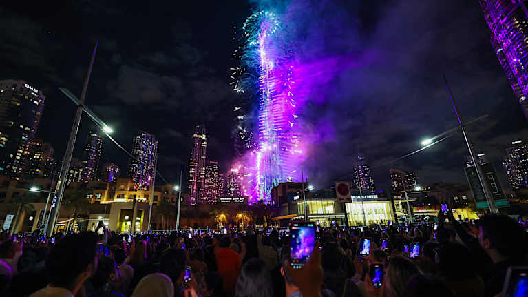 Burj Khalifa loistaa ilotulitteiden valossa. Etualalla on ihmisiä, moni kuvaa kännykällään.