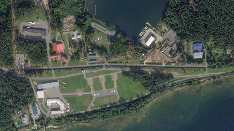 SAtelliittikuvassa näkyy useita rakennuksia helikopterin laskeutumisalusta ympärillä. Rakennusta ympäröi metsikkö sekä vesistö.