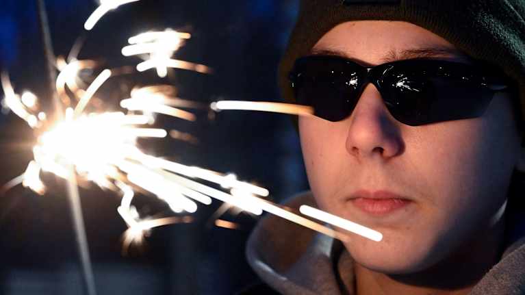 Nuori mies mustissa laseissa ja sädetikku kädessä.