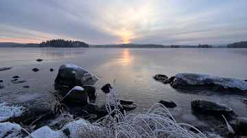 Aurinko laskee jäätyneen järven horisonttiin.