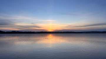 Aurinko laskee ohuesti jäätyneen järven horisonttiin.