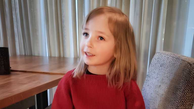 5-vuotias tyttö istuu penkillä. Hänellä on päällään punainen neulepaita, jossa lukee "Kuumaa". 