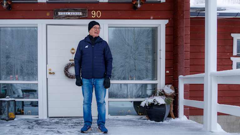 Kari Sinkkonen seisoo kotitalonsa talvisella kuistilla. Talon seinässä numero 90 muistuttaa myös miehen iästä.