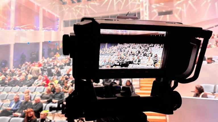 Katsomossa istuu ihmisiä. Etualalla näkyy kameran näyttö.