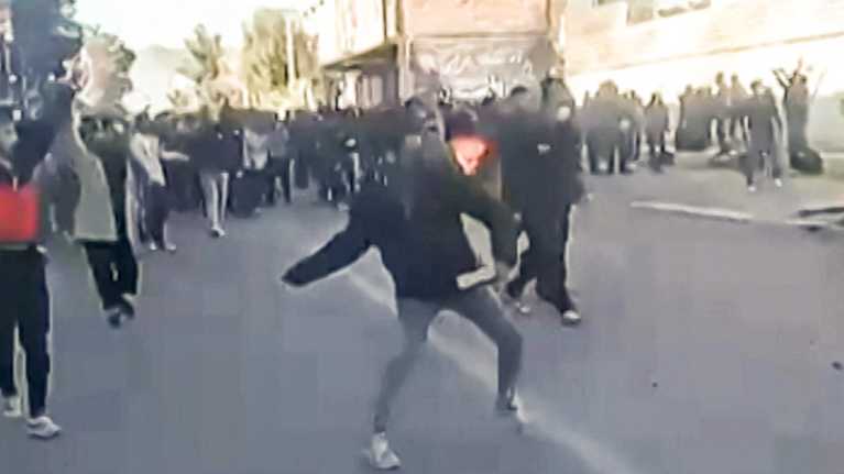 Naamioitunut mielenosoittaja on väkijoukossa käsi ja vartalo heittoasennossa. Kuvassa ei näy mitä hän heittää.