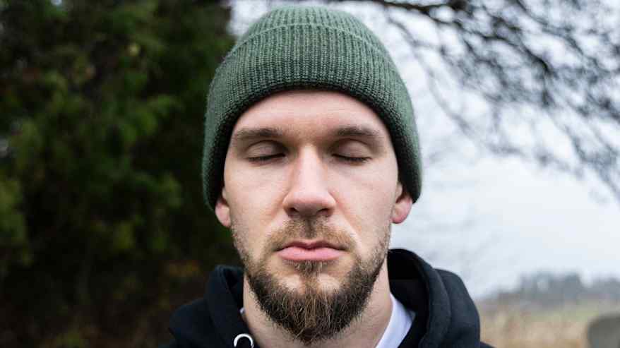 Pipopäinen parrakas mies on lähikuvassa silmät kiinni.