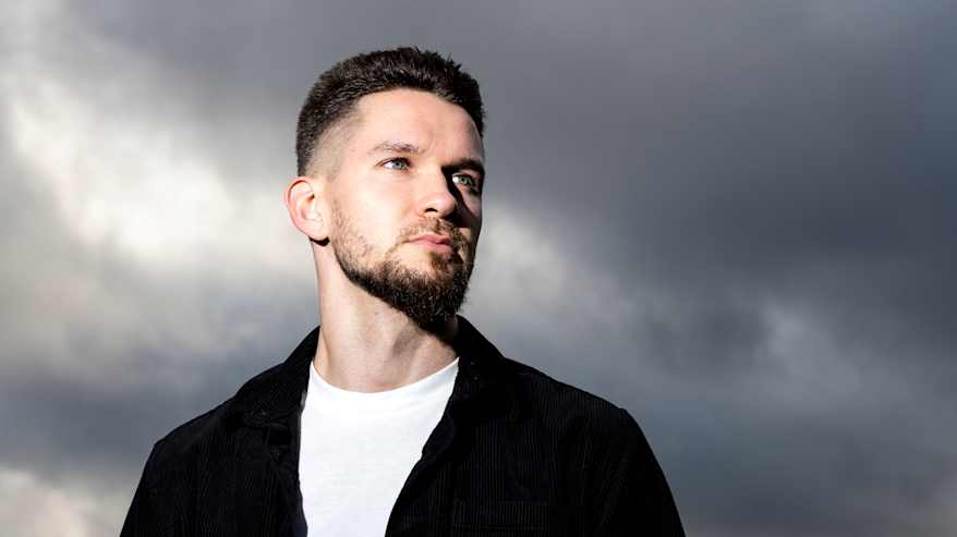 Henkilökuvassa mies hieman alaviistosta kuvattuna tummaa pilvitaivasta vasten.