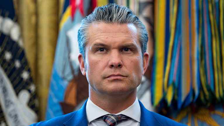 Mies katsoo eteenpäin tilaisuudessa. Takana on lippuja.