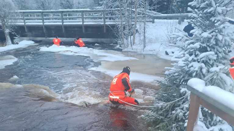 Kolme miestä purkaa hyydepatoa joessa.