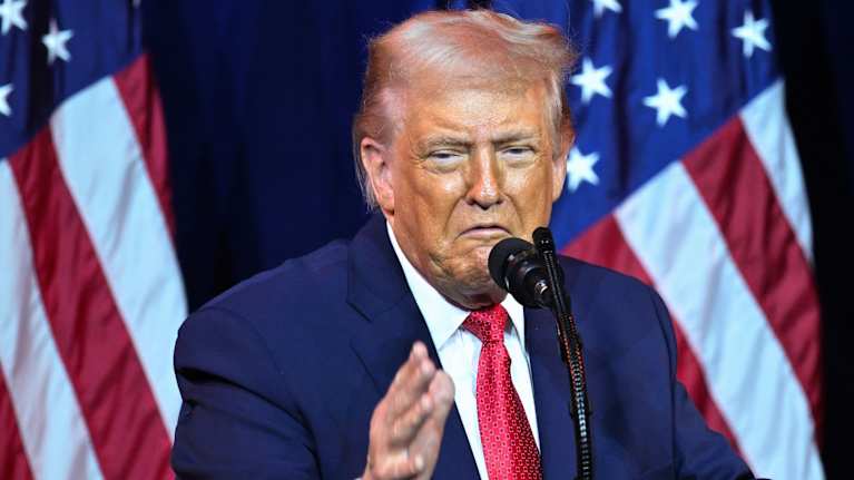 Donald Trump puhuu mikrofoniin ja elehtii kädellään. Taustalla Yhdysvaltain lippu.