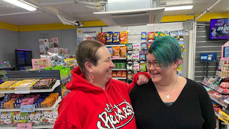 Kaksi ihmistä seisoo vierekkäin ja katsoo tyytyväisinä toisiaan keskellä kioskia. 