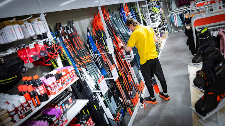 Myyjä asettelee suksia urheiluliikkeen telineisiin.