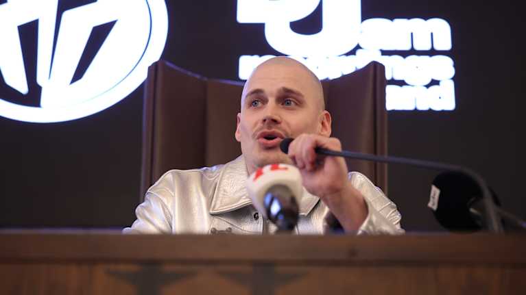 Rap-artisti Gettomasa puhuu mikrofoniin tiedotustilaisuudessa. 