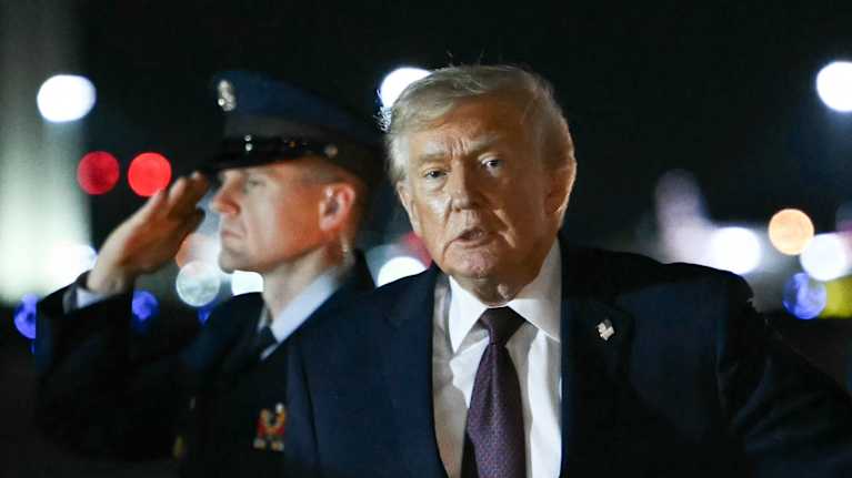 Donald Trump på flygplats med militärperson i bakgrunden.