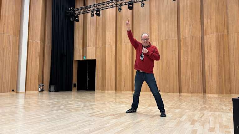 Mies seisoo lavalla toinen käsi ylhäällä ja laulaa.