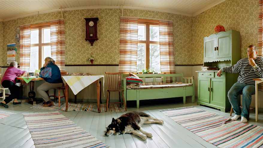 Vanhan talon tuvassa kaksi naista istuu kahvipöydän ääressä ja koira makaa lattialla.