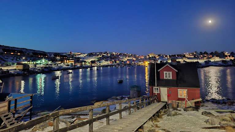 Punainen talo rannalla, kuu paistaa, on pimeää Aasiaatin kaupungissa Grönlannissa.