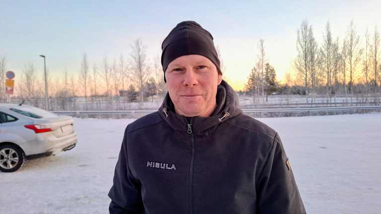 Pipopäinen mies talvisessa autojen pysäköintipaikassa.