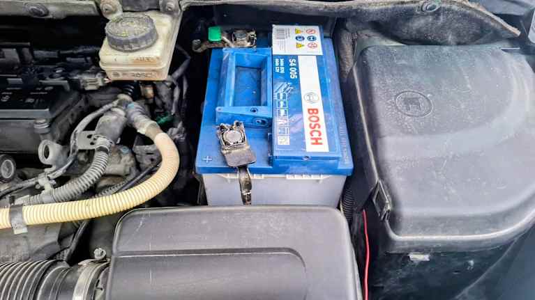 Kuvassa näkyy auton moottoritila, jossa on Bosch-merkkinen akku. Akkua ympäröi useita letkuja ja johtoja.