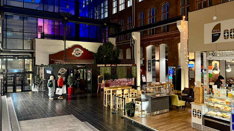 Korkeassa sisätilassa on kahvilan pöytiä ja liiketiloja.