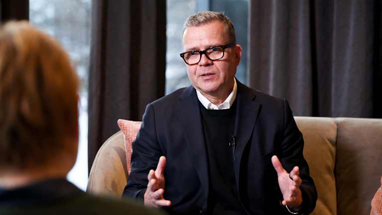 Petteri Orpo istuu sohvalla tumma puku päällä.