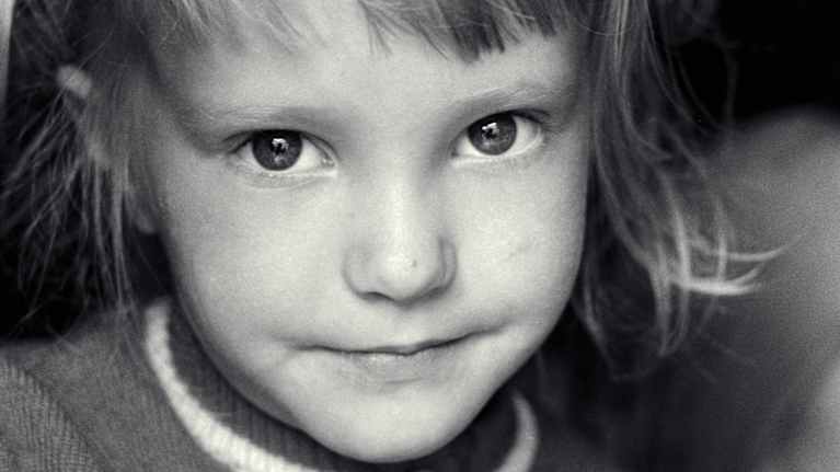 Tyttö katsoo kameraan ja hymyilee vienosti mustavalkoisessa valokuvassa.