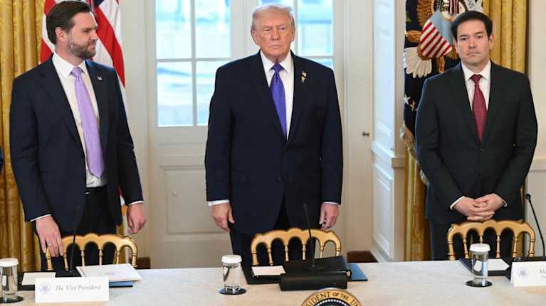 Kolme miestä seisoo tuolien takana kokouspöydän ympärillä Valkoisessa talossa.