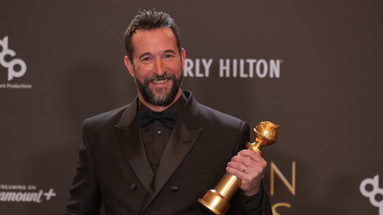 Näyttelijä Noah Wyle katsoo hymyillen kameraan kädessään juuri voittamansa Golden Globe -palkinto.