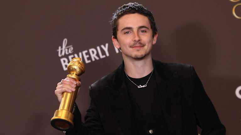 Näyttelijä Timothée Chalamet katsoo hymyillen kameraan ja nostaa oikealla kädellään Golden Globe -palkintoaan.